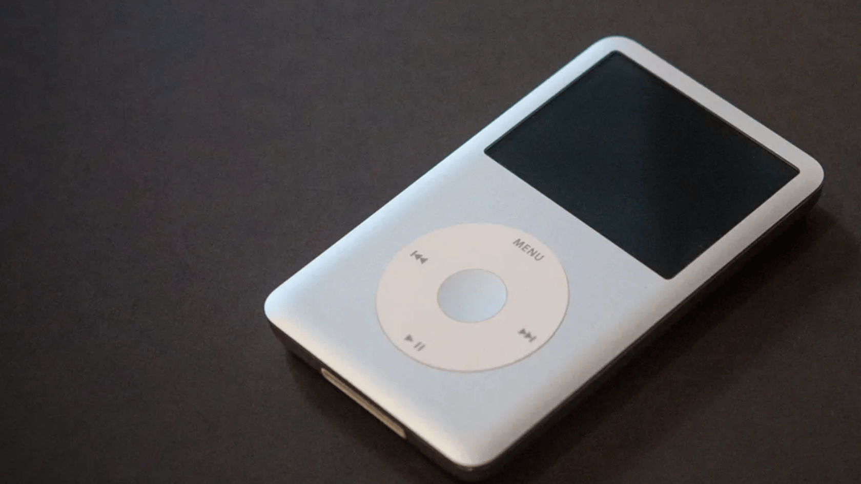 Silver ipod with circular control wheel and dark screen resting on a dark surface.