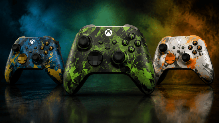 Three custom Xbox controllers with blue, green, and orange camo splatters on a dark reflective surface.
