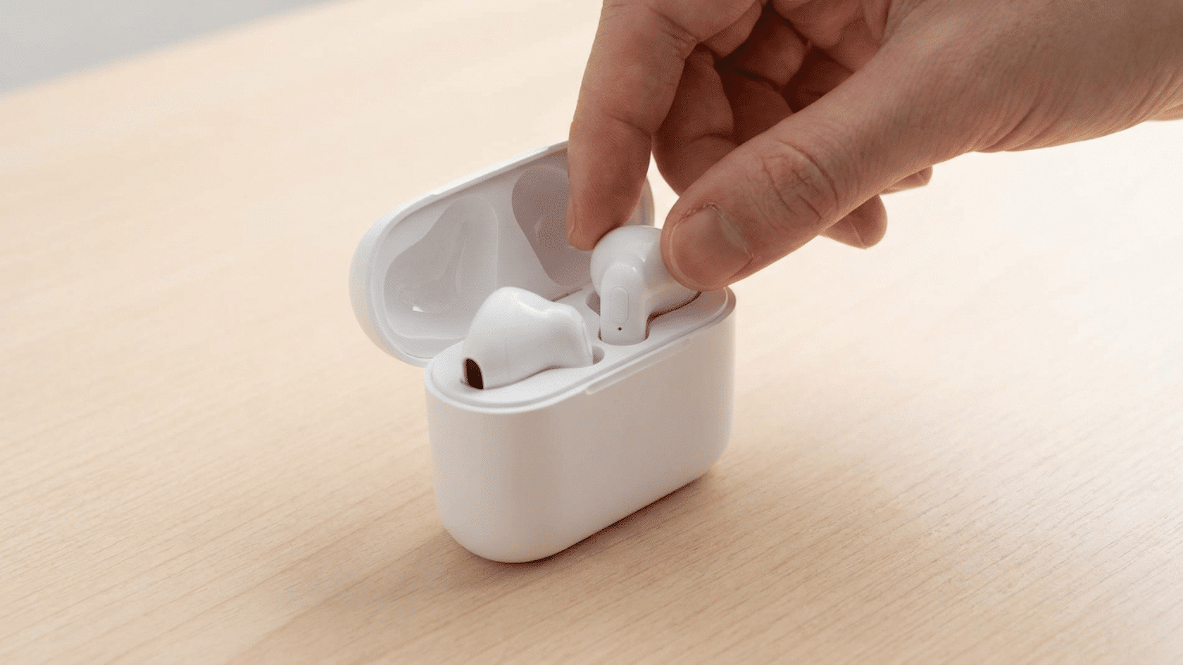 A hand placing AirPods into the open slots of their charging case