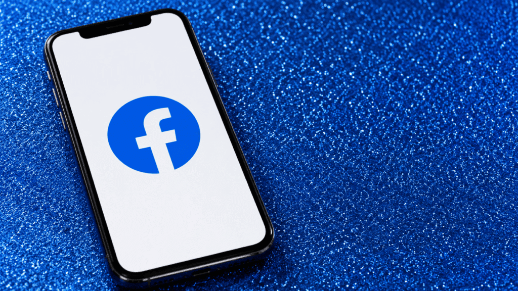 Smartphone showing Facebook logo on screen placed on blue glitter background with diagonal phone orientation front view