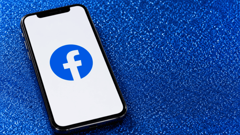 Smartphone showing Facebook logo on screen placed on blue glitter background with diagonal phone orientation front view