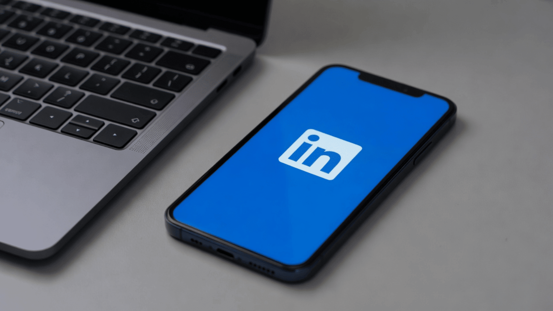 Smartphone beside laptop displaying LinkedIn logo on blue screen