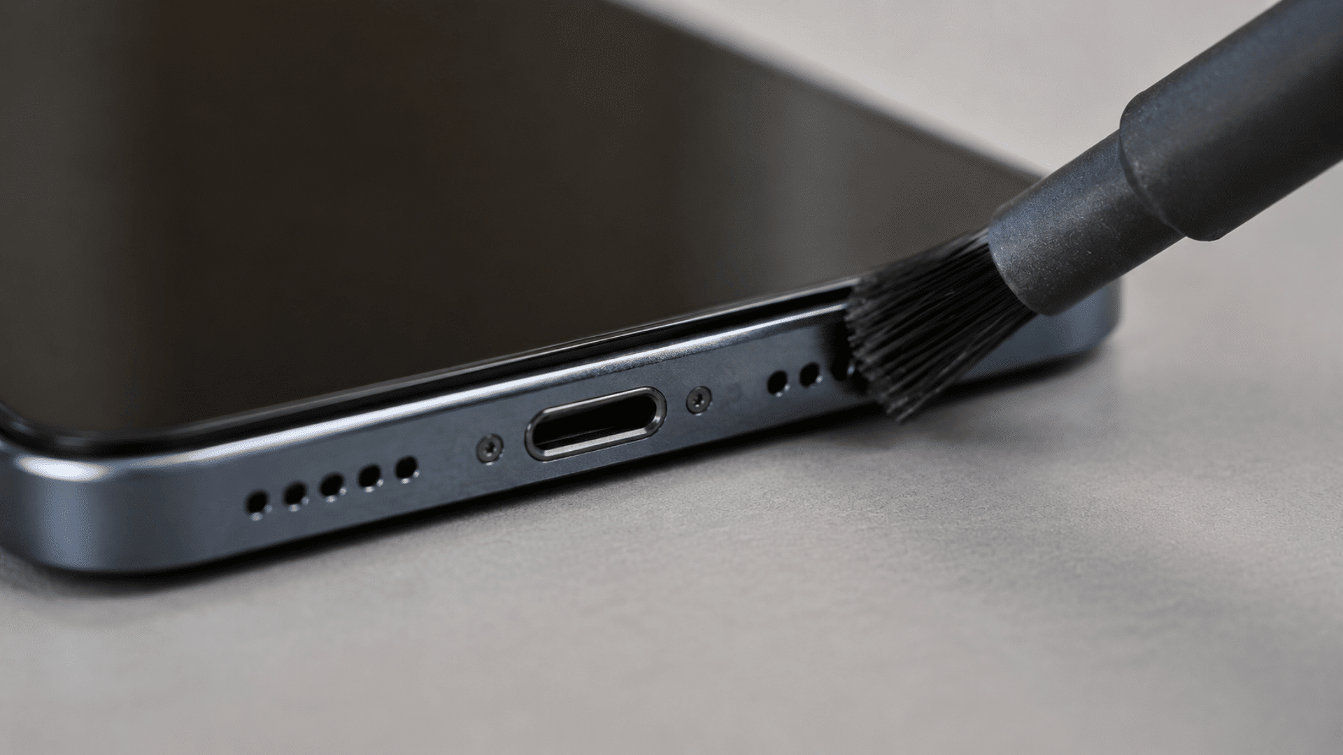 Soft brush cleaning smartphone microphone port on phone edge close-up view