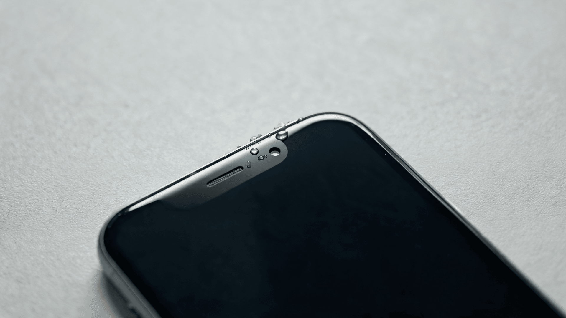 Smartphone with small water droplets near microphone openings on flat surface close-up vie