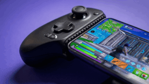 Black gaming controller beside a smartphone displaying a colorful mobile game on a purple background