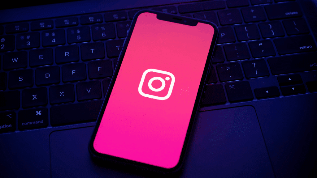 Smartphone displaying Instagram logo on a dark keyboard with pink screen glow and blue ambient lighting.