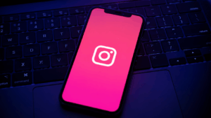 Smartphone displaying Instagram logo on a dark keyboard with pink screen glow and blue ambient lighting.