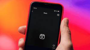 Hand holding a red smartphone displaying Instagram Reels creation screen against a colorful gradient background.