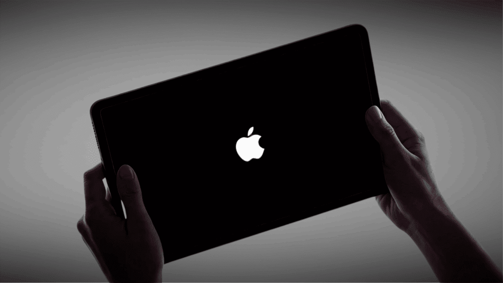 Hands holding an iPad with a black screen displaying the Apple logo during startup.