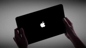 Hands holding an iPad with a black screen displaying the Apple logo during startup.