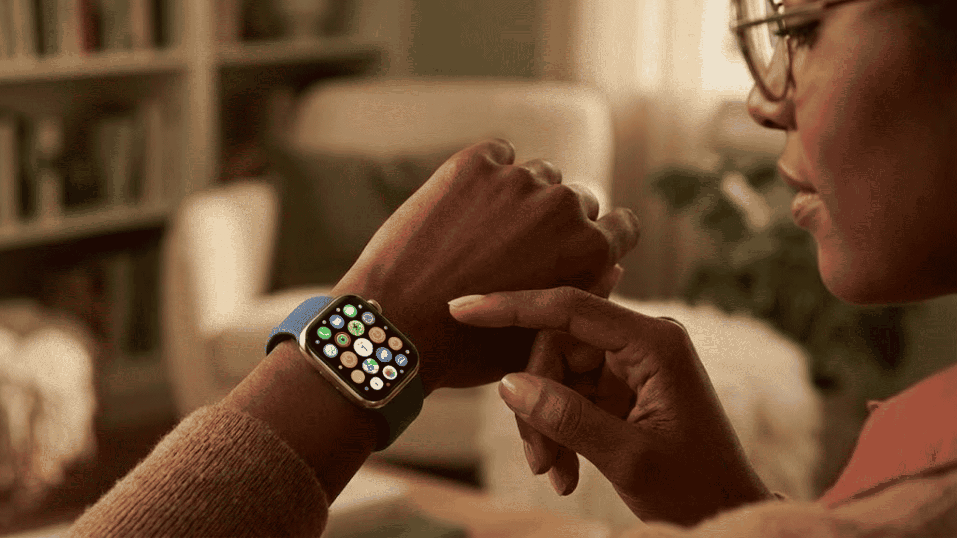 Close-up of a woman with dark skin wearing an Apple Watch with a blue band, navigating app icons.