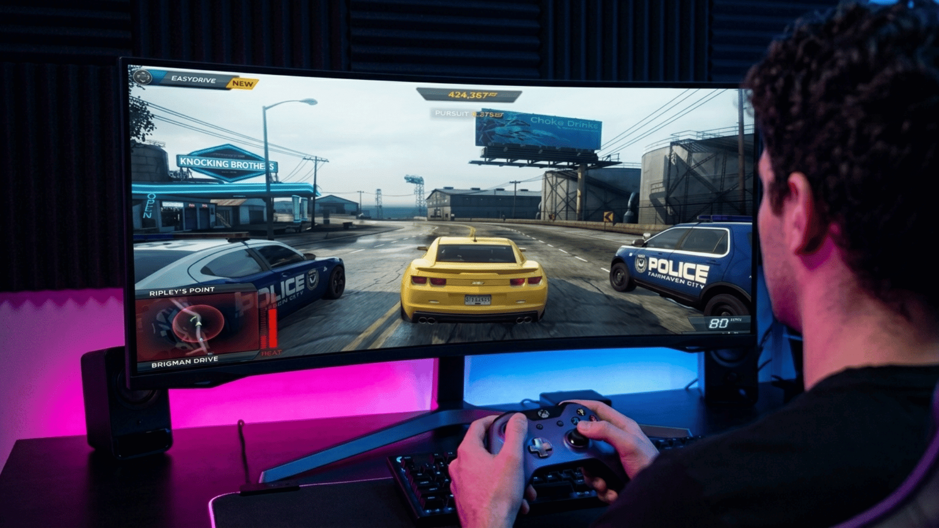 Person playing a racing video game with a controller at a desktop gaming setup.