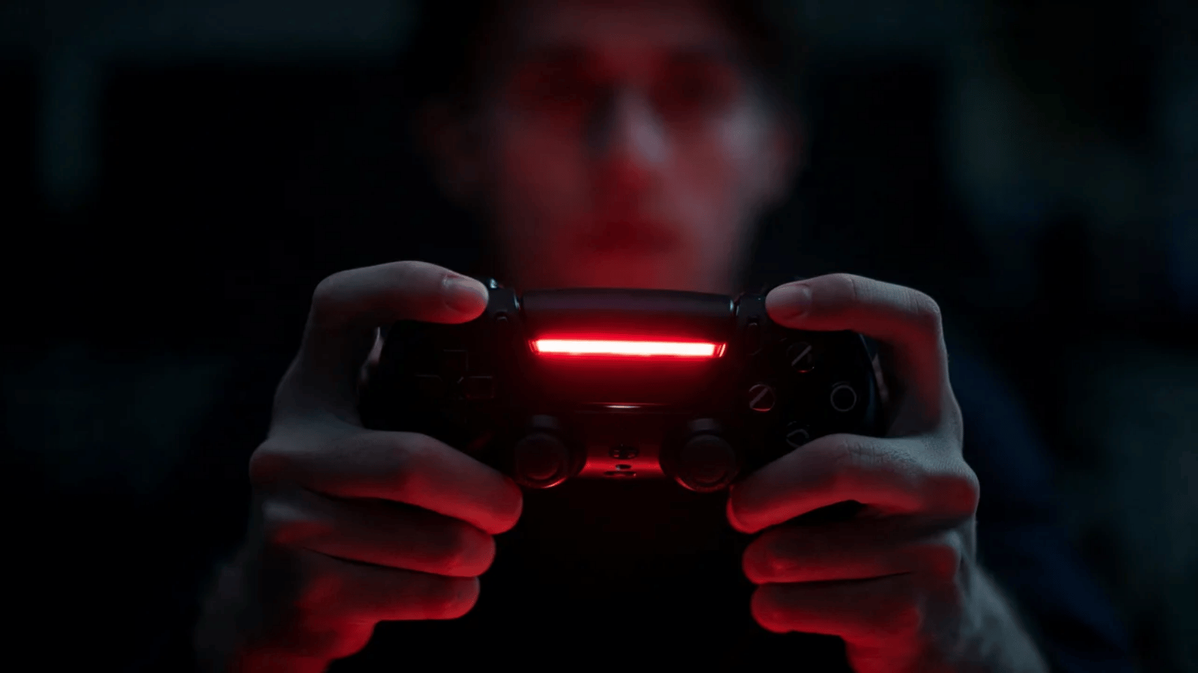 Person holding a gaming controller with red light glowing in a dark room during gameplay.
